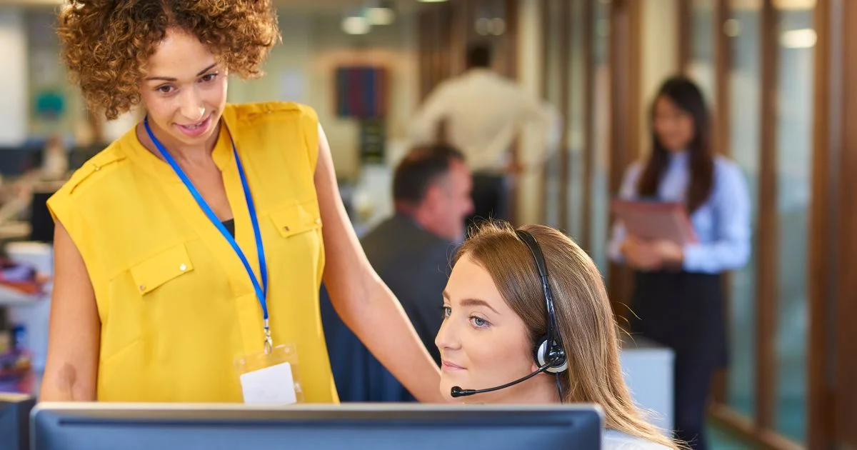 Manager training new employee wearing headset at office computer.
